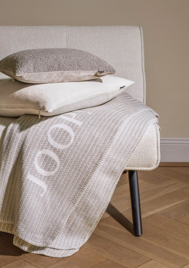 Плед JOOP! WOVEN CRÈME, кремовый, наброшен на кушетку с подушками, вышитая надпись JOOP!