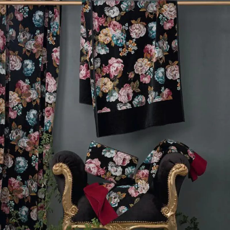 Шенилловые полотенца Feiler ROSE DREAM с пышными цветами на чёрном поле висят на штанге и лежат на золочёном кресле