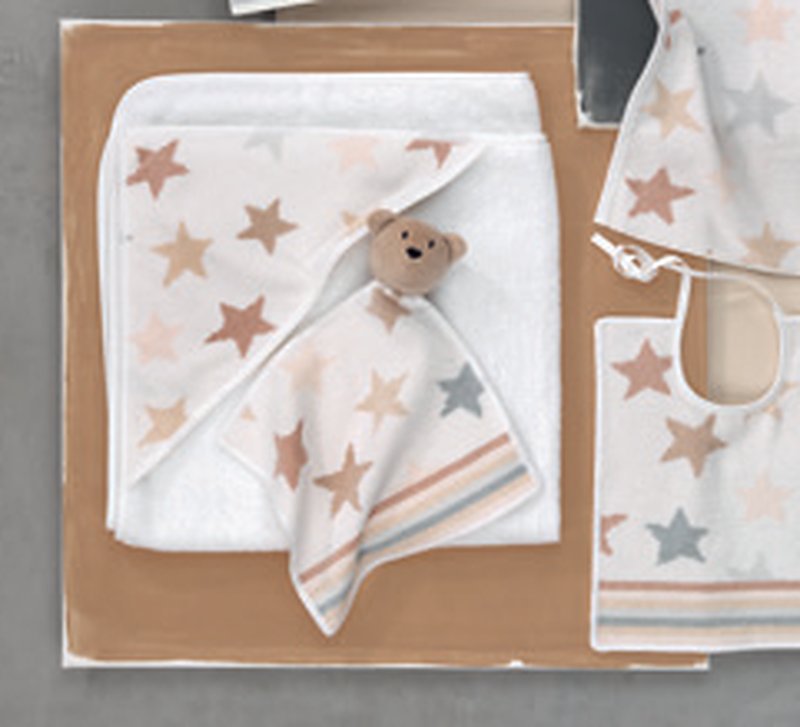 Изделия Feiler Mini STARS & STRIPES разложены на светло-коричневой и серой поверхности: полотенце с капюшоном, салфетка-соска с головой медвежонка и нагрудник — белое шенилловое поле с бежевыми и серыми звёздами и полосами